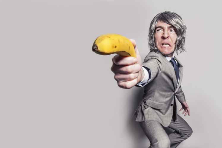 man in gray suit jacket holding yellow banana fruit while making face